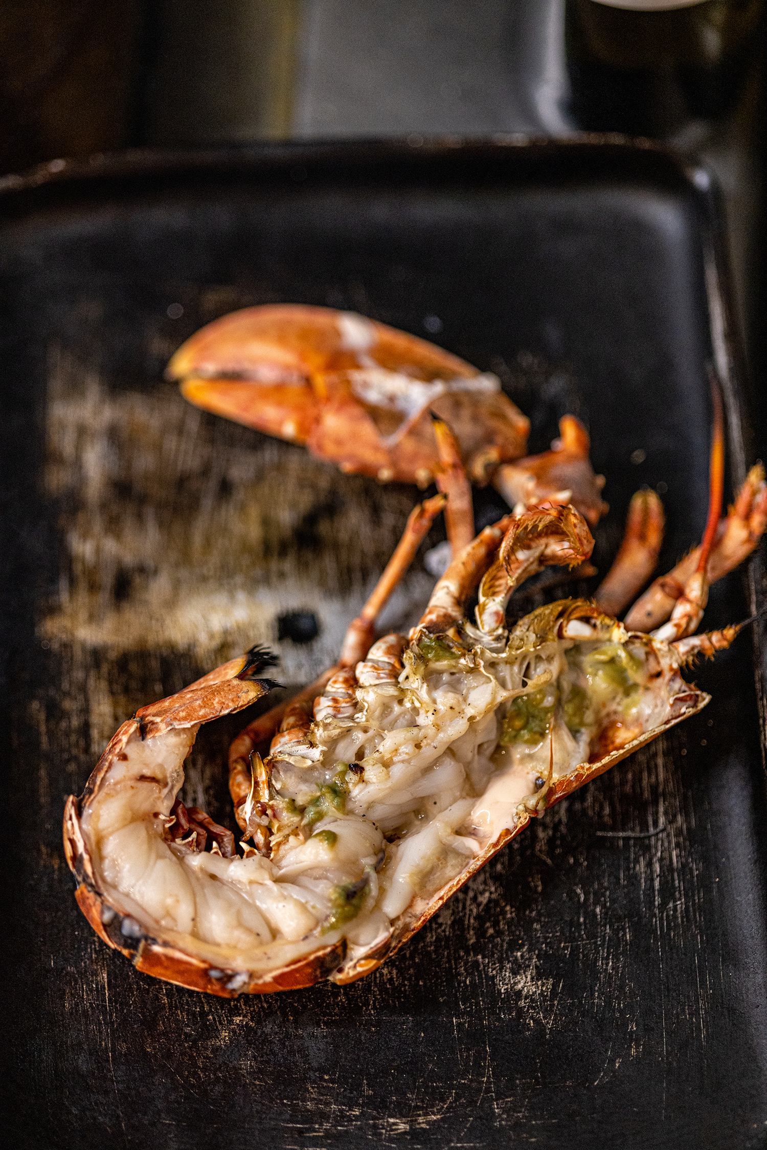 Lobster tail with stuffing or sauce inside, placed on a black grill or pan.