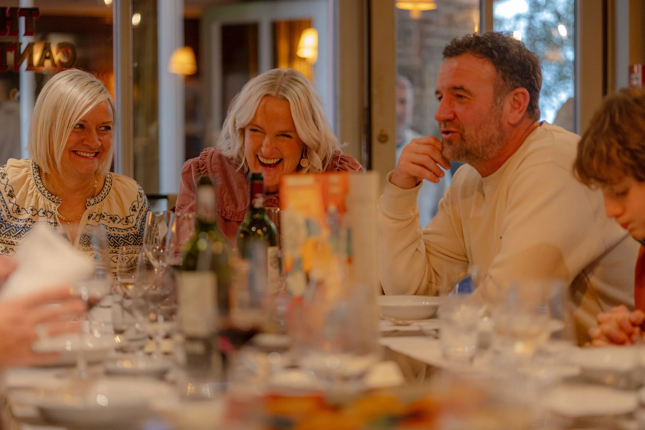 People sitting around a dining table laughing and enjoying a meal at a restaurant or cafe.