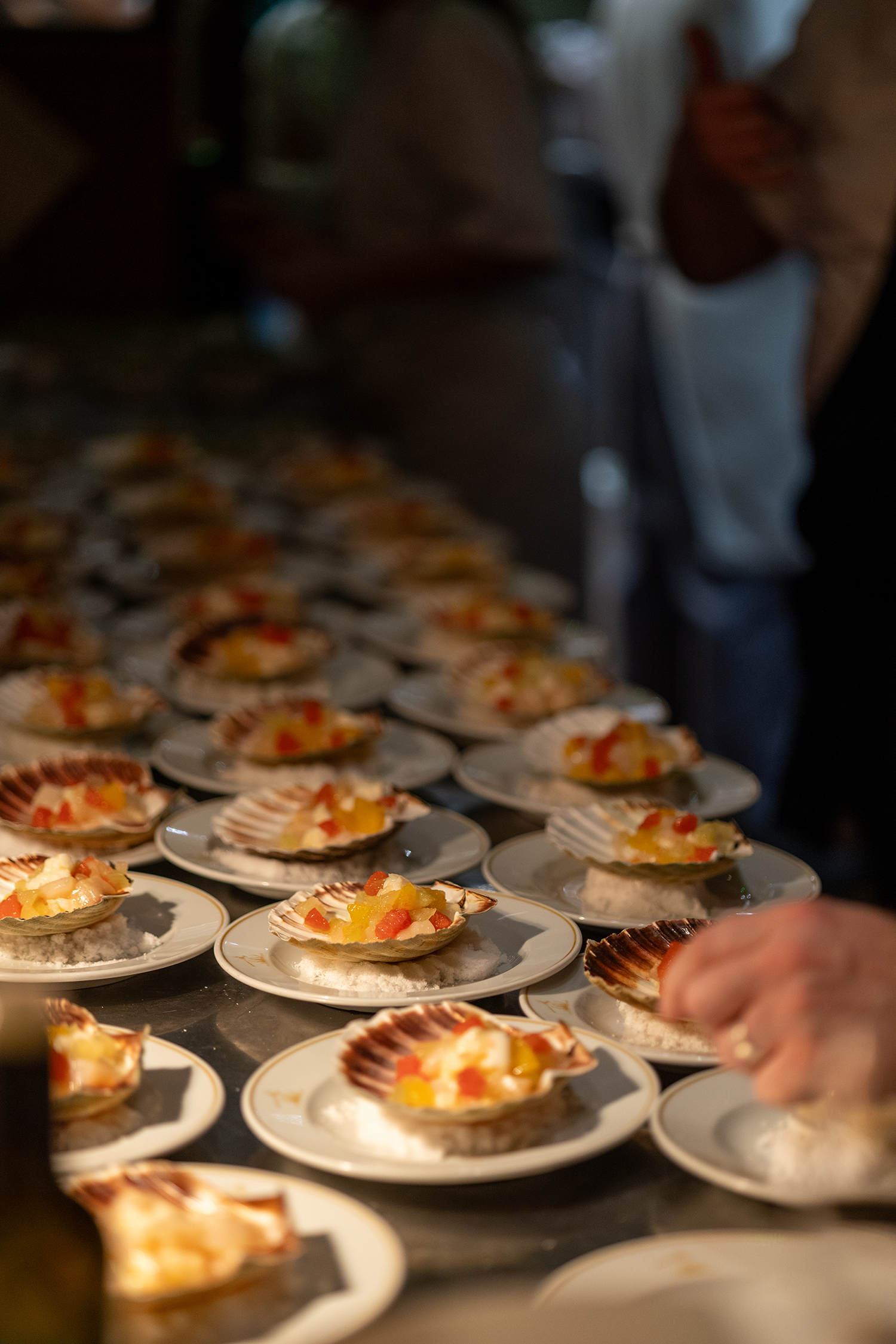 Close-up of several small plates of food featuring scallops topped with pineapple and red peppers, arranged on a table.