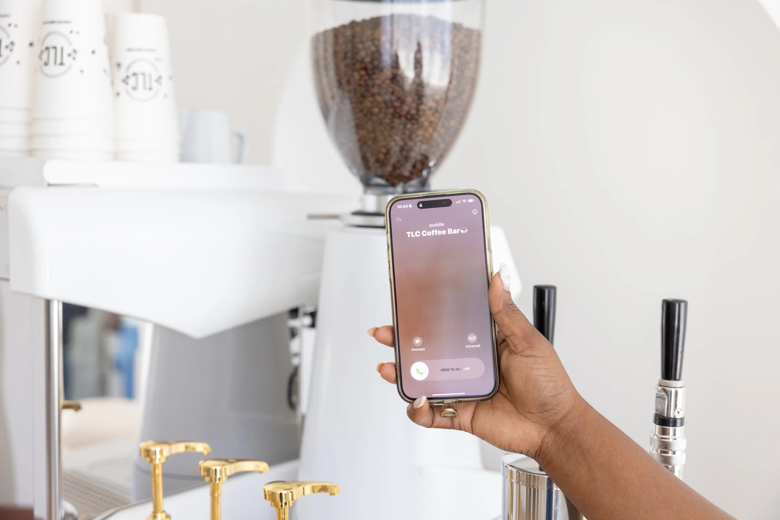 Person holding a smartphone with an incoming call from TLC Coffee Bar in a coffee shop environment.