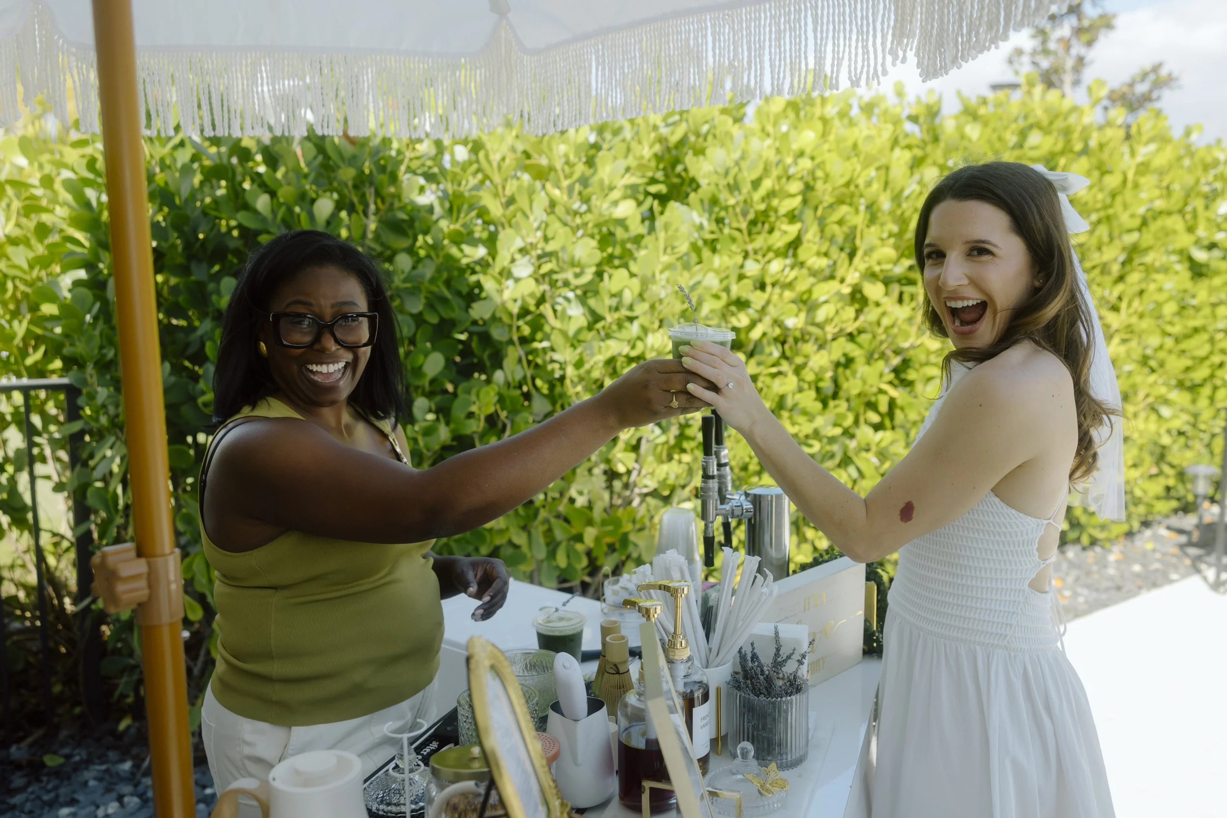 Two women at an outdoor celebration clinking drinks and smiling.
