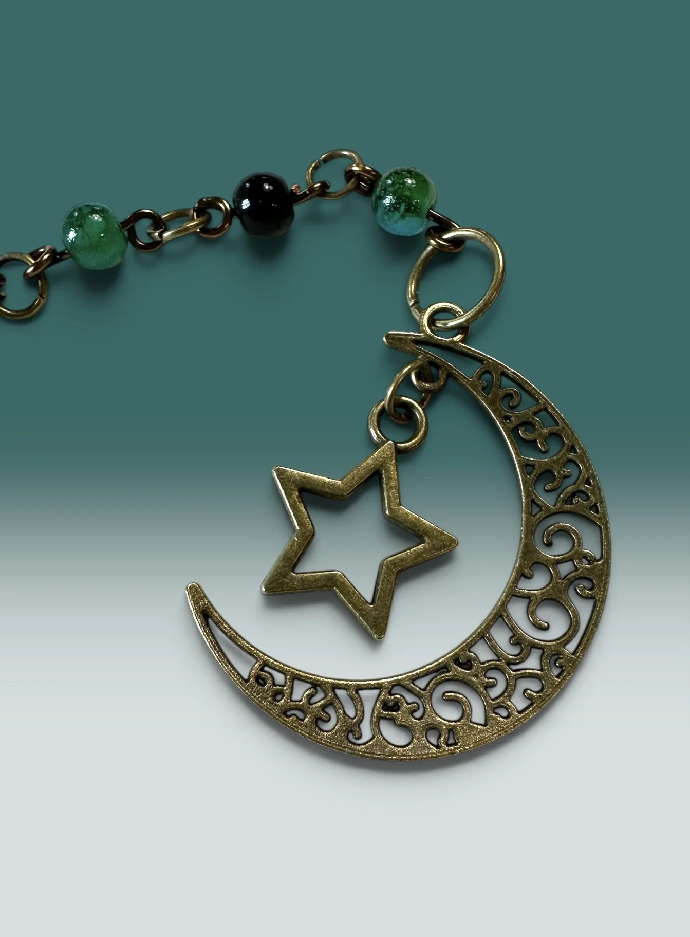 An antiqued bronze crescent moon and star charm accented with deep green and black glass beads.
From the Velvet Midnight Wander line — celestial-inspired charms in rich, nighttime tones.