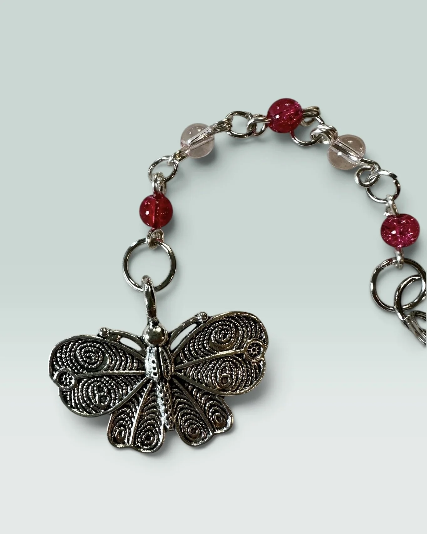Handmade children's charm featuring a silver filigree butterfly with red and pink glass beads — part of the Poppy collection. Hypoallergenic clasp hardware.