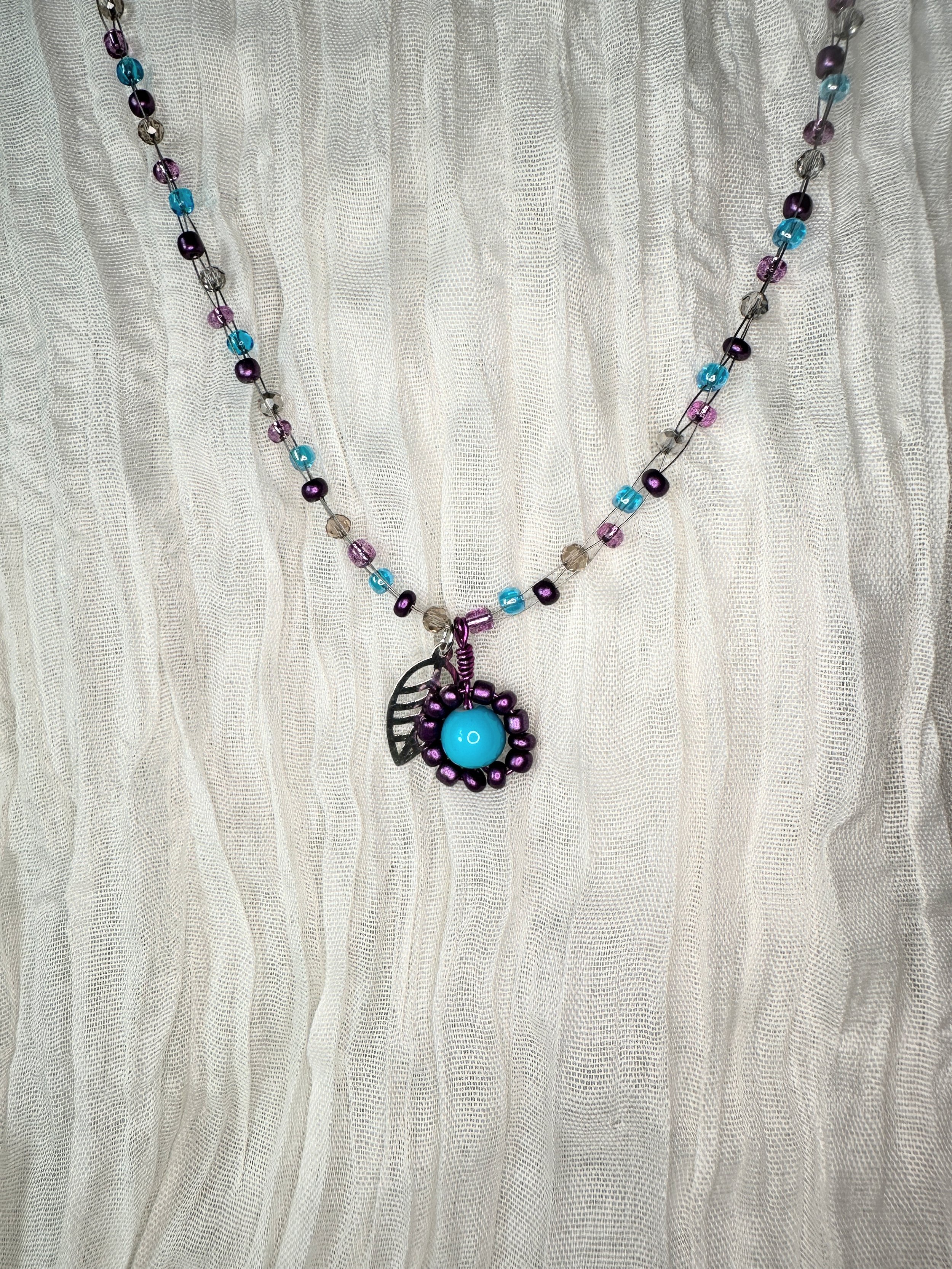 Handmade children's necklace featuring a beaded flower charm with a turquoise center and silver leaf accent, paired with purple and teal glass beads — part of the Bluebell collection. Hypoallergenic hardware, hand-strung.
