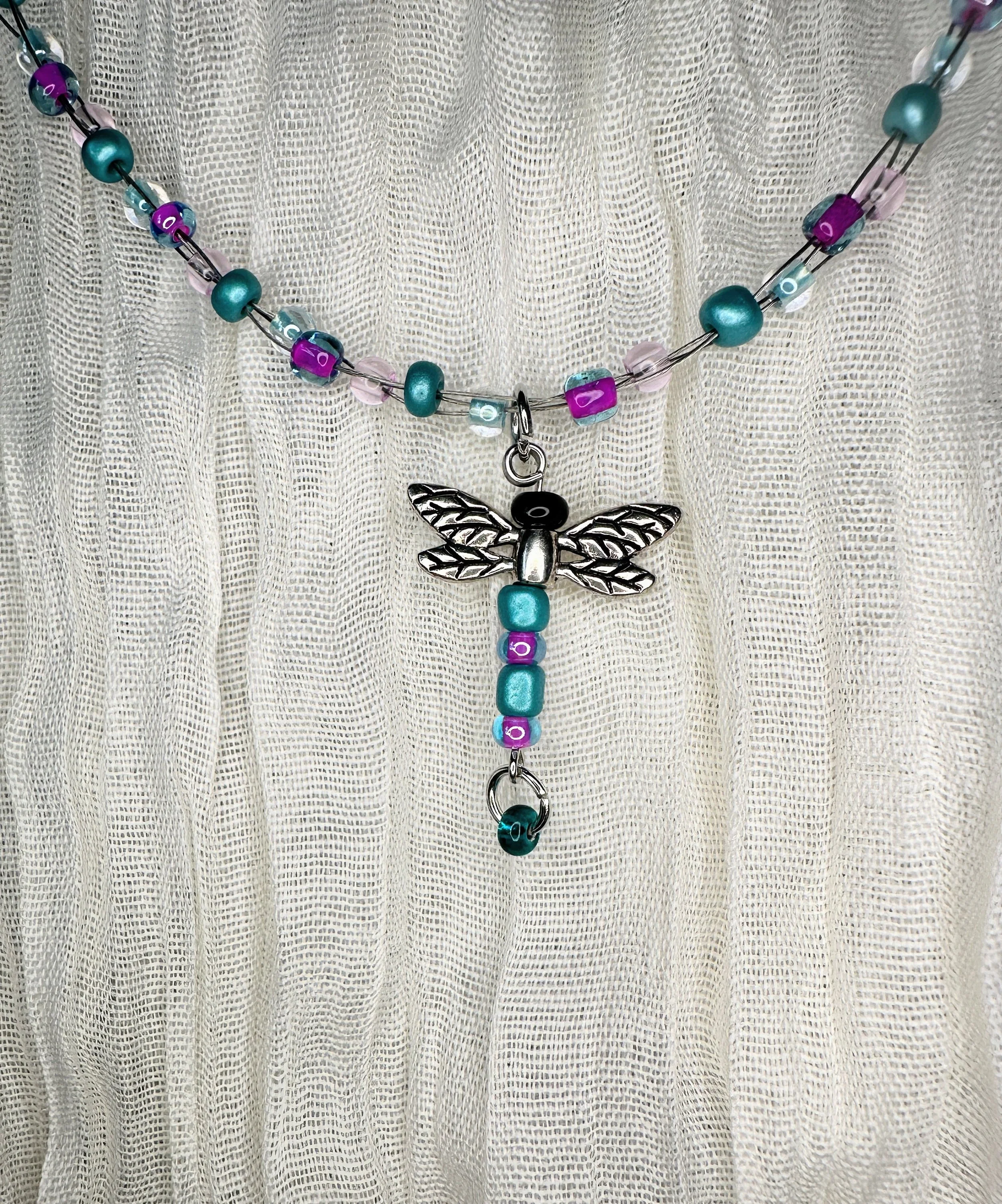 Handmade children's necklace featuring a silver dragonfly charm with teal, purple, and pink glass beads — part of the Hyacinth collection. Hypoallergenic hardware, hand-strung.