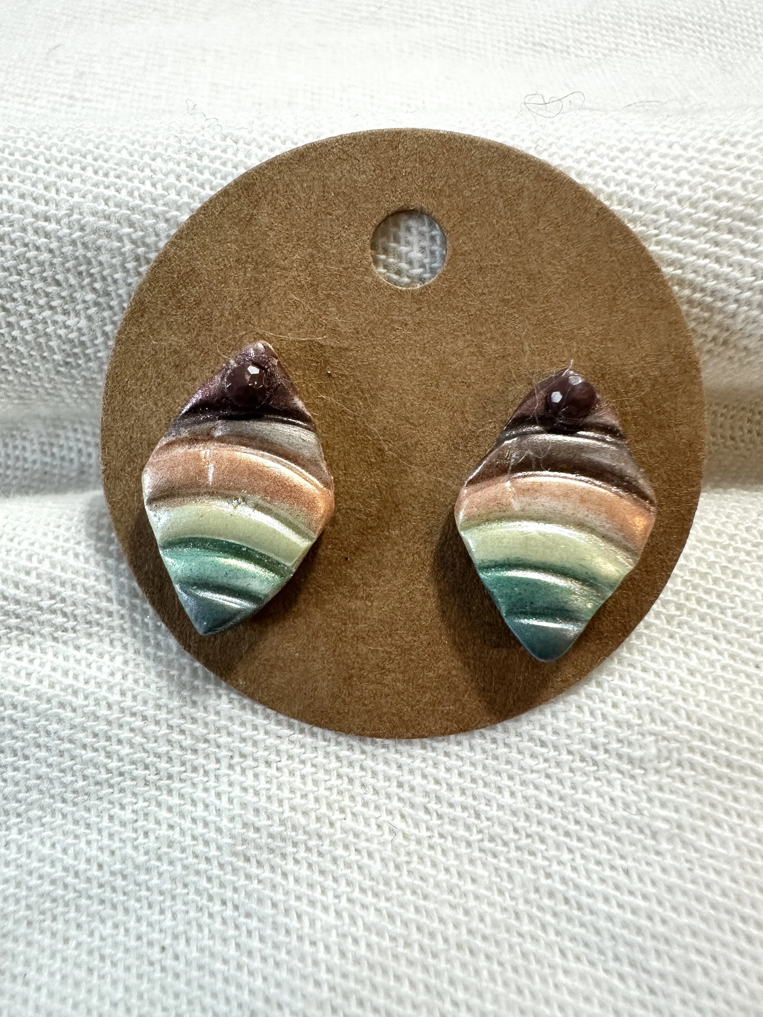 Handmade sculpted stud earrings featuring a hand-formed clay design in a copper-to-teal ombre finish with a purple stone accent — part of the Hyacinth collection. Hypoallergenic earring posts.