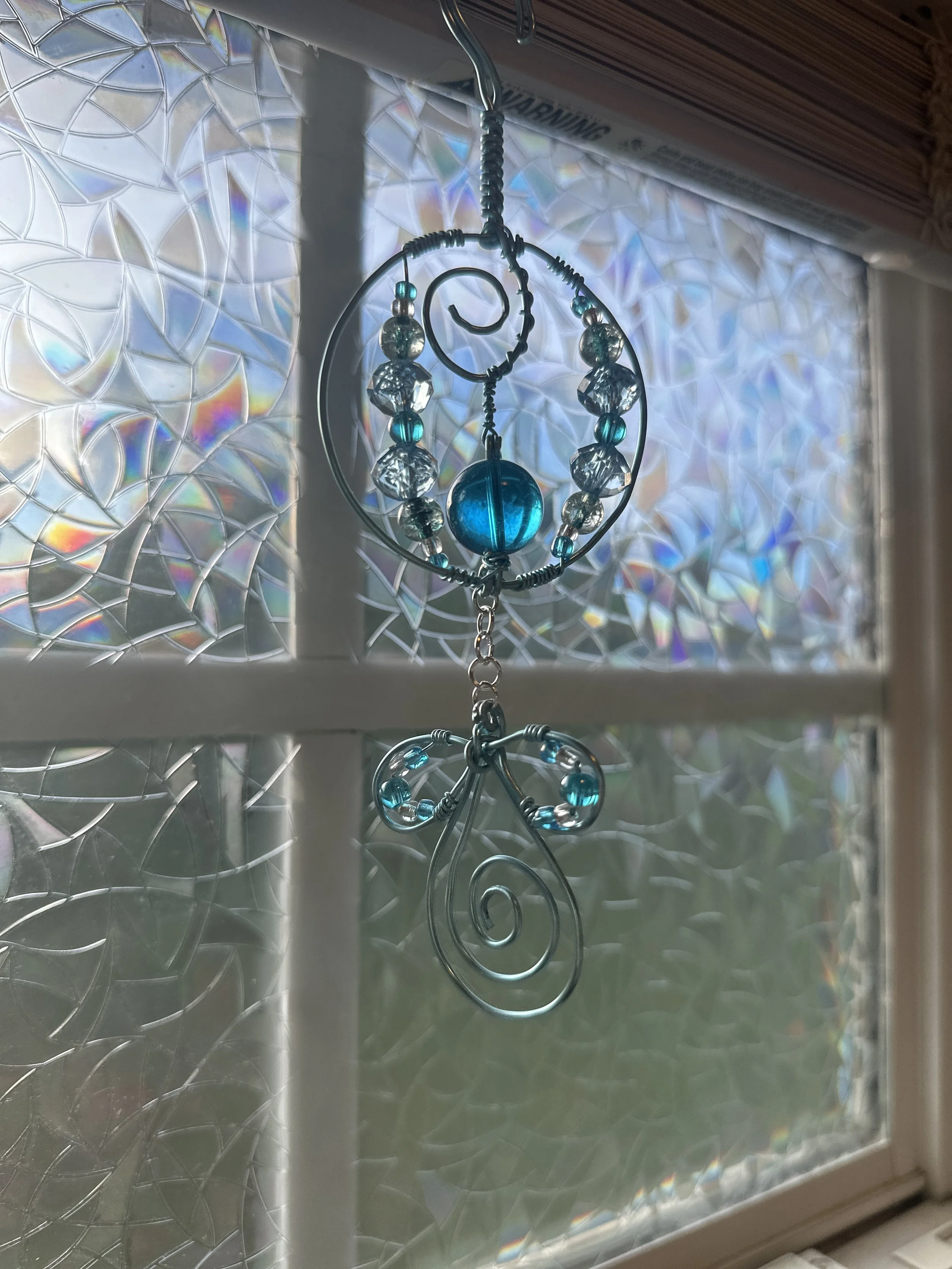 A wire-wrapped circular car charm in cool blue and silver tones with faceted glass beads and a dangling spiral drop.
Part of the Still Water Wander series — calming, water-inspired charms made for the road.