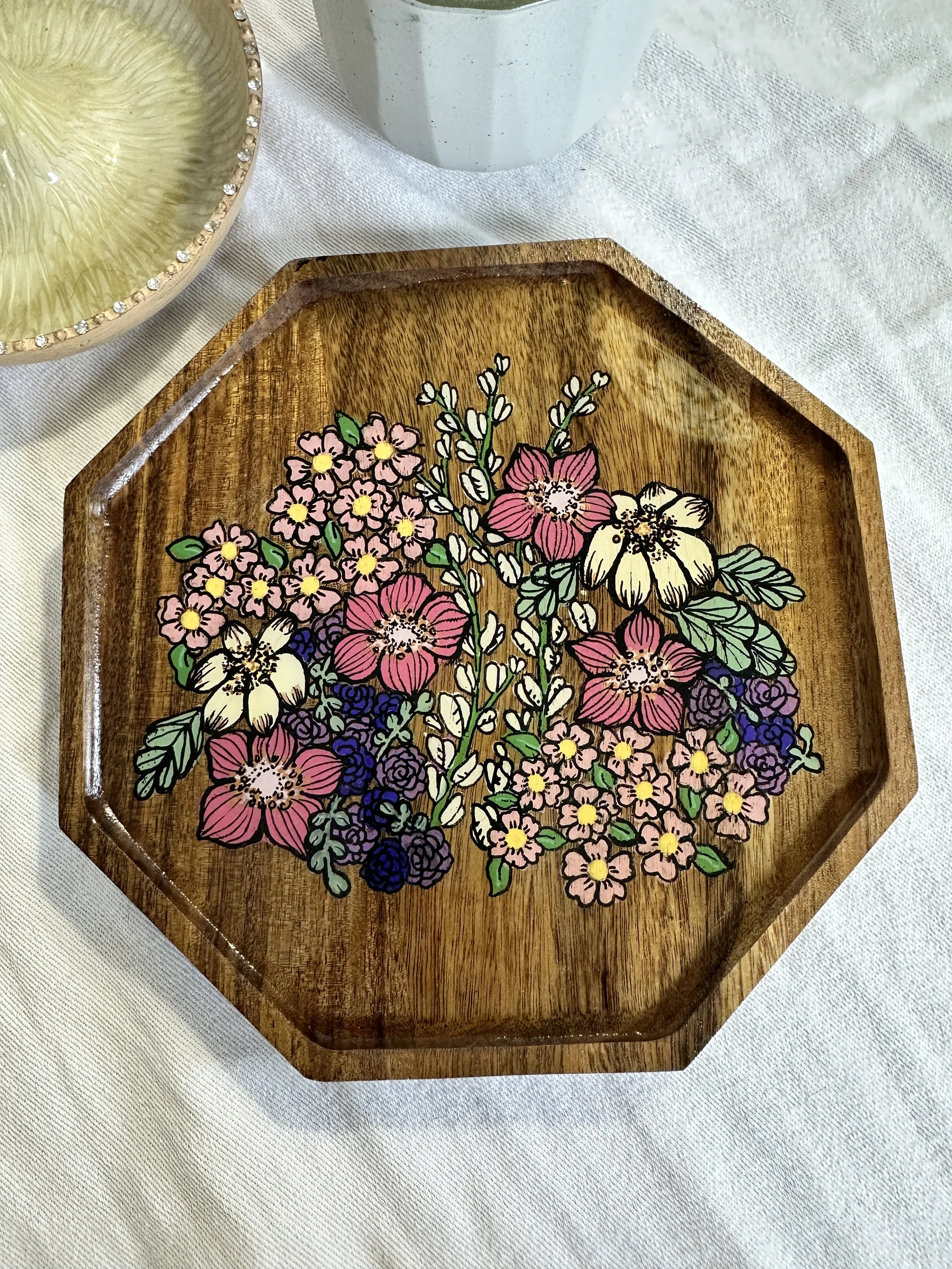 An octagonal wood catch-all tray hand-painted with a lush multicolor floral bouquet in pink, cream, and purple.
Also from the Petal & Wing line — designed to hold jewelry, keys, or trinkets while echoing the collection's floral theme.
