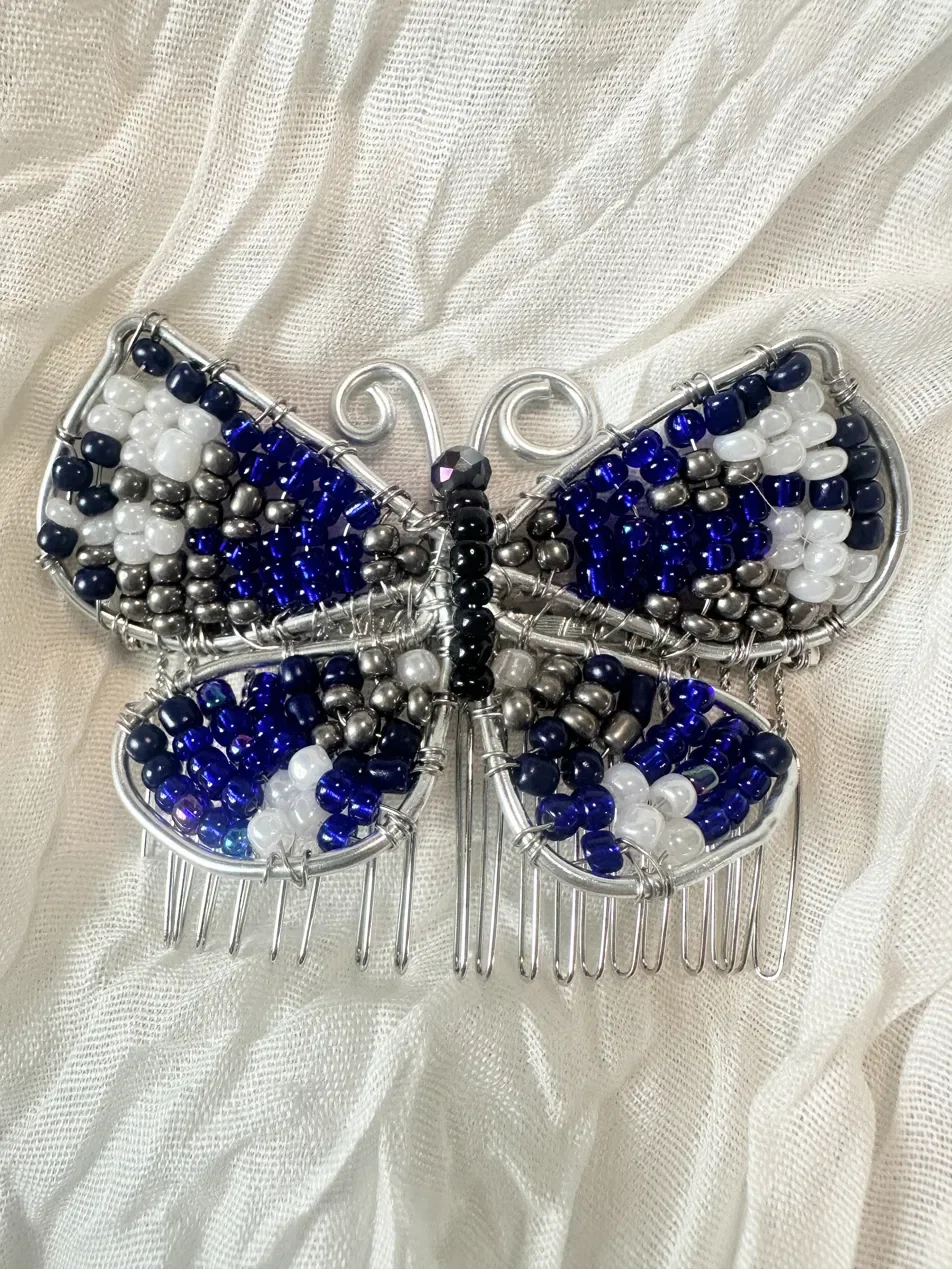 Handmade artisan hair comb featuring a beaded butterfly design in navy, white, and silver glass beads — part of the Deep Blue Lake collection. Hand-beaded with hypoallergenic hardware.