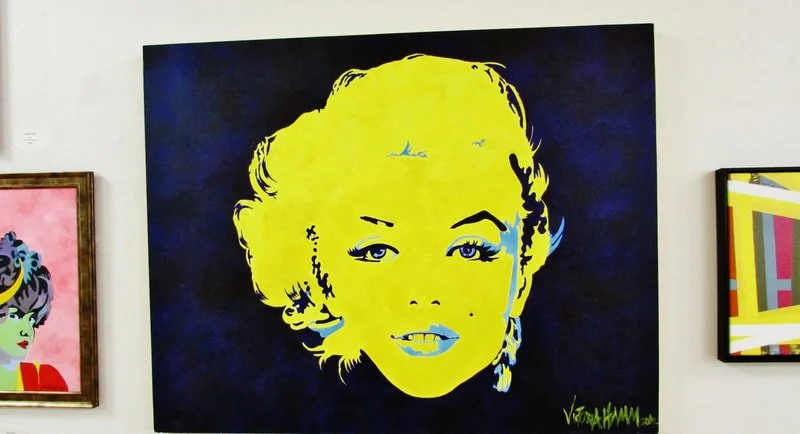 Pop art portrait of Marilyn Monroe with yellow face, blue eyes, and black hair, on a black background.