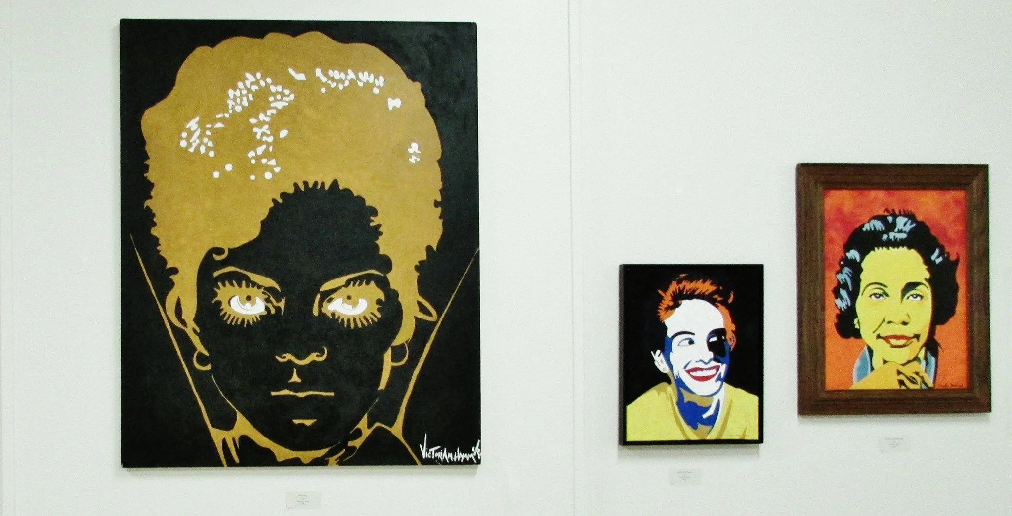 Four pop art portraits on display, featuring a young girl with an afro hairstyle, a woman with short hair smiling, a woman with short hair and an animated expression, and a woman with curly hair smiling. The portraits use vibrant colors and bold outl