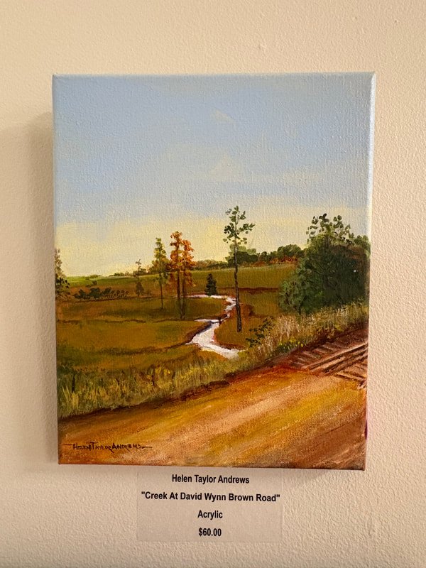 A landscape painting of a creek flowing through fields with trees, under a blue sky, displayed on a wall.