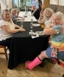 A group of older women sitting around a table, enjoying drinks and smiling.