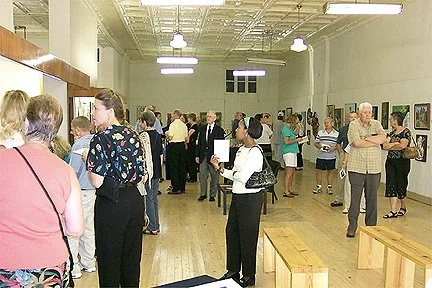 People walking and viewing art in an art gallery with wooden benches.