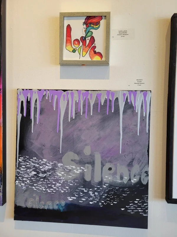 An art display with a small framed colorful abstract painting titled 'Love' at the top and a larger abstract painting below it with purple and gray tones, featuring white drip effects and a partially visible word 'silence'.