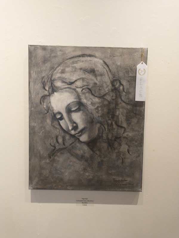 A monochrome charcoal or pencil drawing of a woman with closed eyes and a gentle expression, her head tilted down slightly, with wavy hair surrounding her face, displayed on a wall in an art gallery. A white gallery tag hangs from the top right corne
