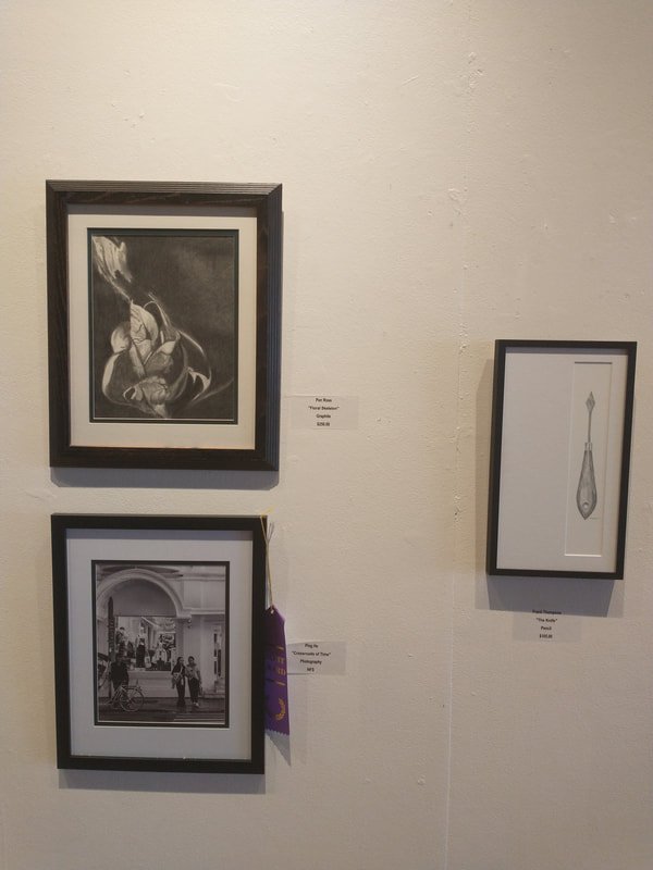 Black and white framed artwork and photos hanging on a white gallery wall. The top left features an abstract drawing, the bottom left shows a street scene with people, and the right has a minimalist image of a fountain pen.