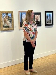 A woman with long hair stands in an art gallery looking at framed photographs on the wall.