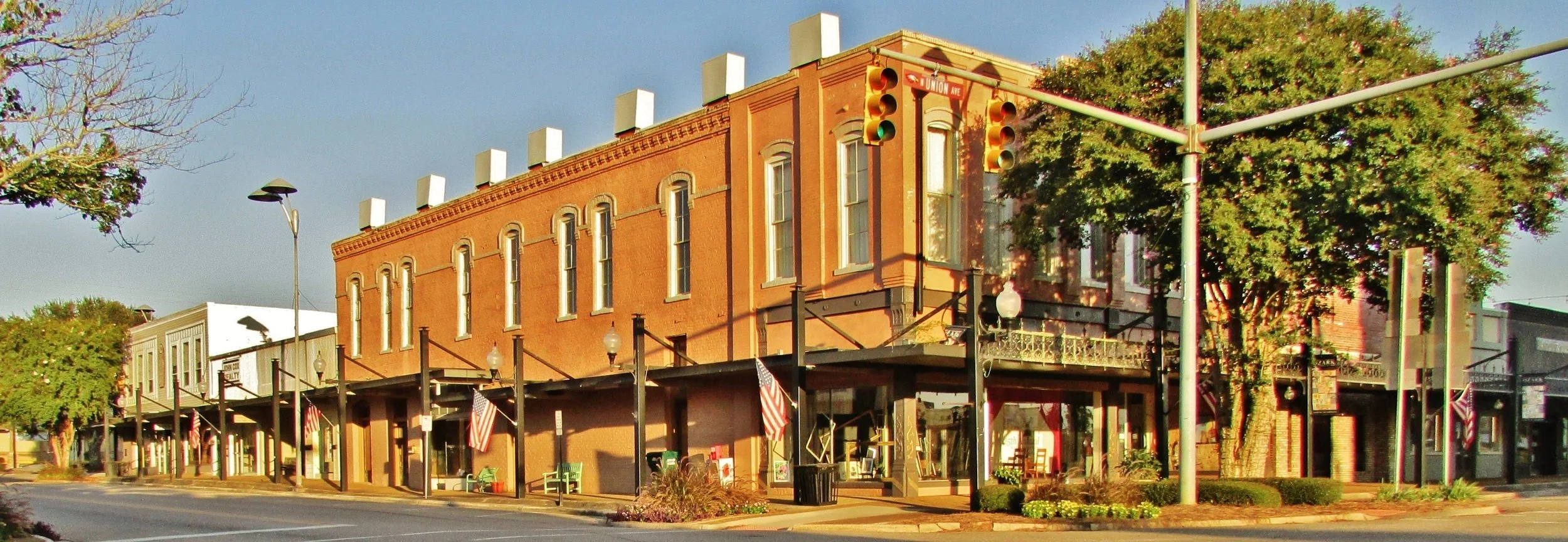 Historic red brick building on a city street corner with American flags and streetlights, under a clear sky with trees lining the sidewalk.