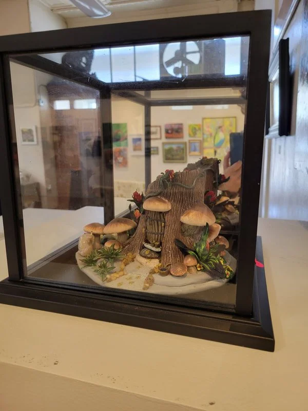 A diorama of a mushroom forest with various mushrooms, plants, and foliage inside a glass display case.