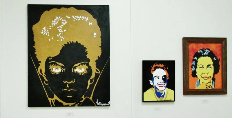 Three colorful pop art portraits of famous women displayed on a white gallery wall, featuring large expressive faces with bold colors and outlines.