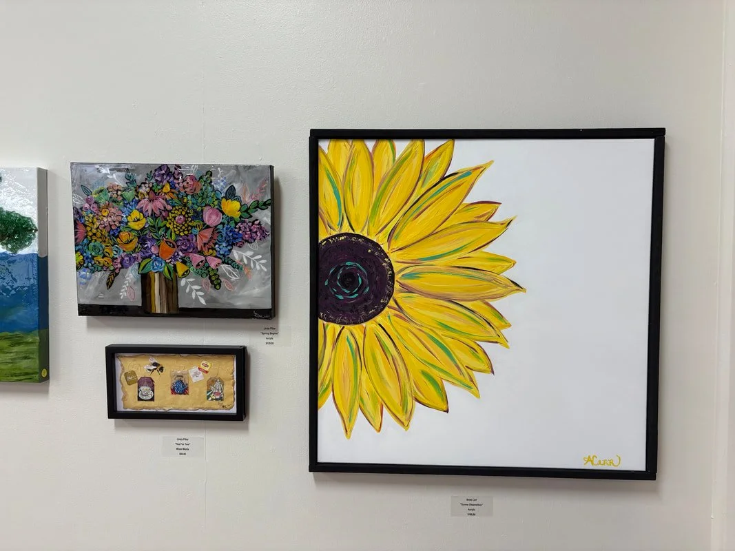Gallery wall featuring a large sunflower painting, a colorful floral tree painting, and small framed artworks.