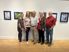 Five people standing in front of artwork displayed on a gallery wall.