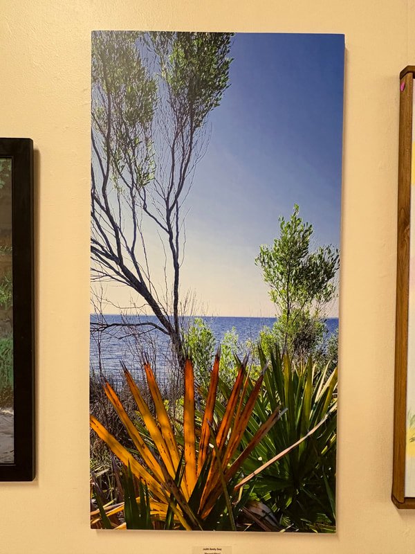 A landscape painting of trees near a body of water with a clear blue sky in the background.