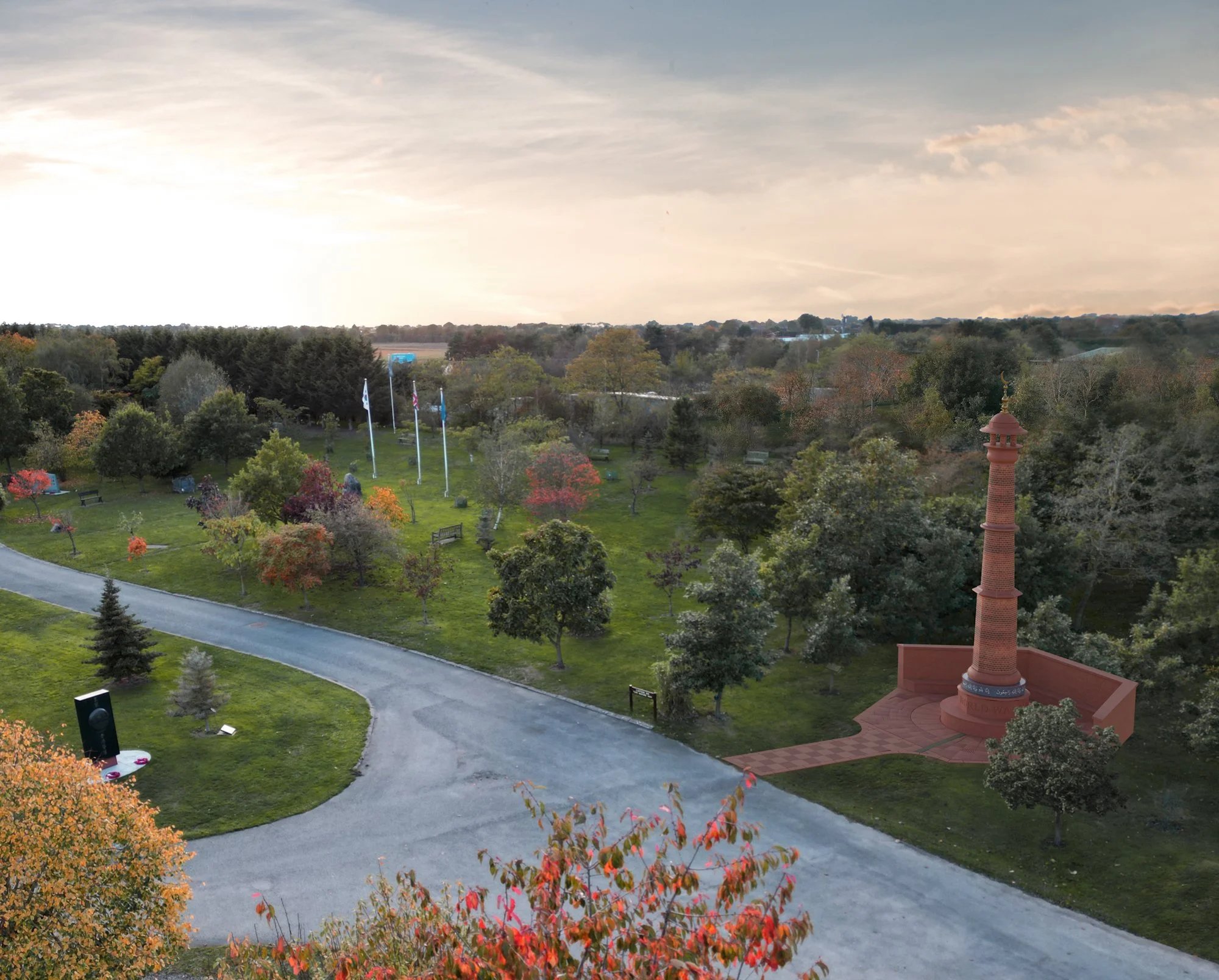 A park with colorful autumn trees, a winding gravel path, flags, with the propsed Muslim memorial, and a cloudy sky.