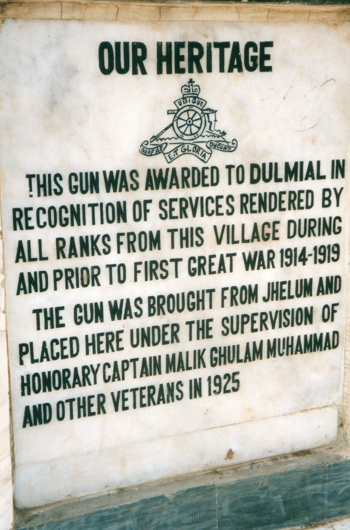 A historical plaque titled "Our Heritage" explaining that a gun was awarded to Dulmal in recognition of services during and before World War I, brought from Jhelum and placed under supervision of Honorary Captain Malik Ghulam Muhammad in 1925.