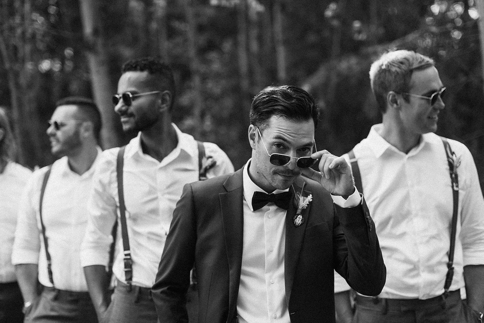 a groom walking in front of his groomsmen looking over his sunglasses-thin-bordered