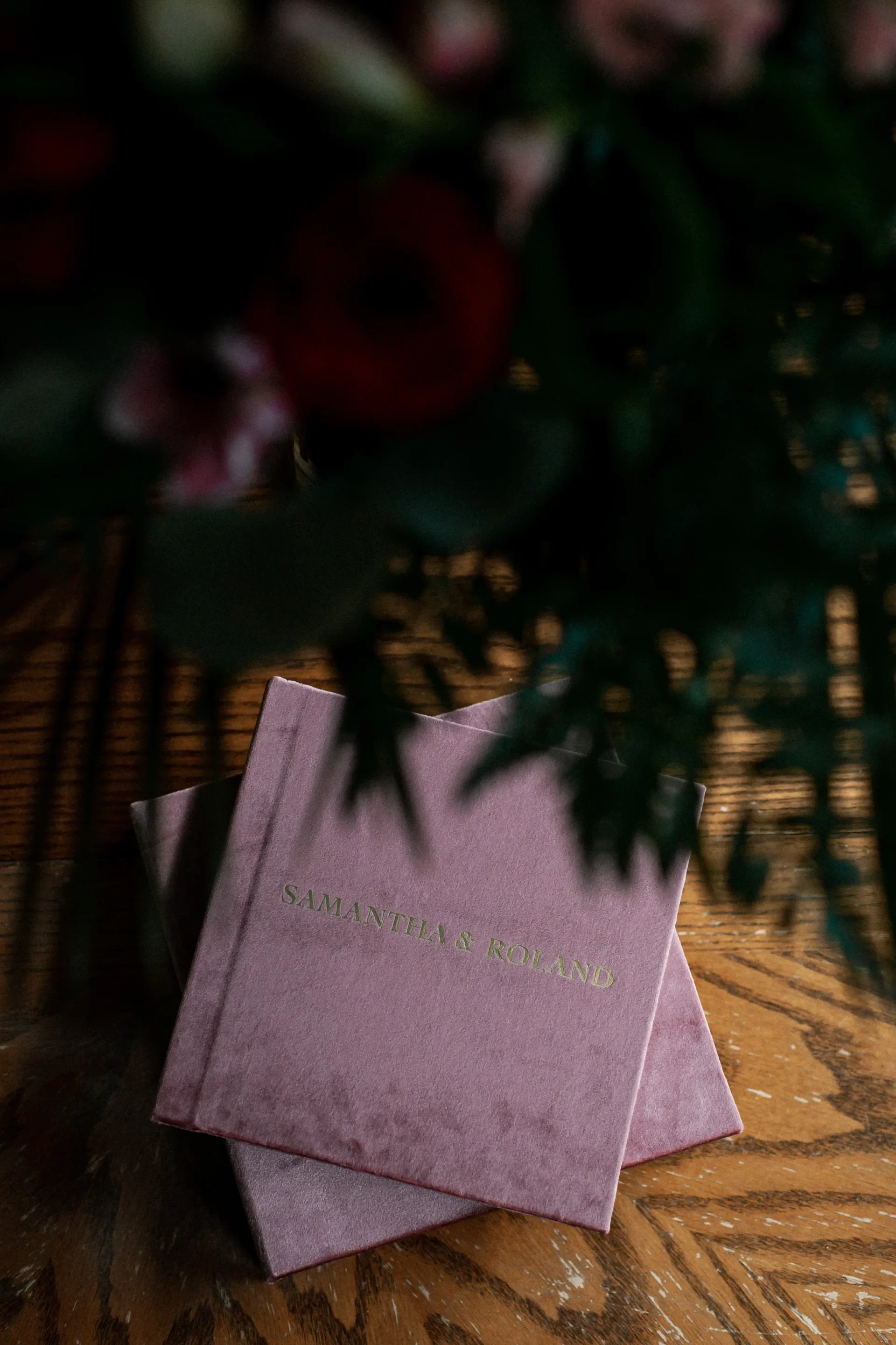 Two blush pink velvet wedding photo albums stacked on a wood table-thin-bordered