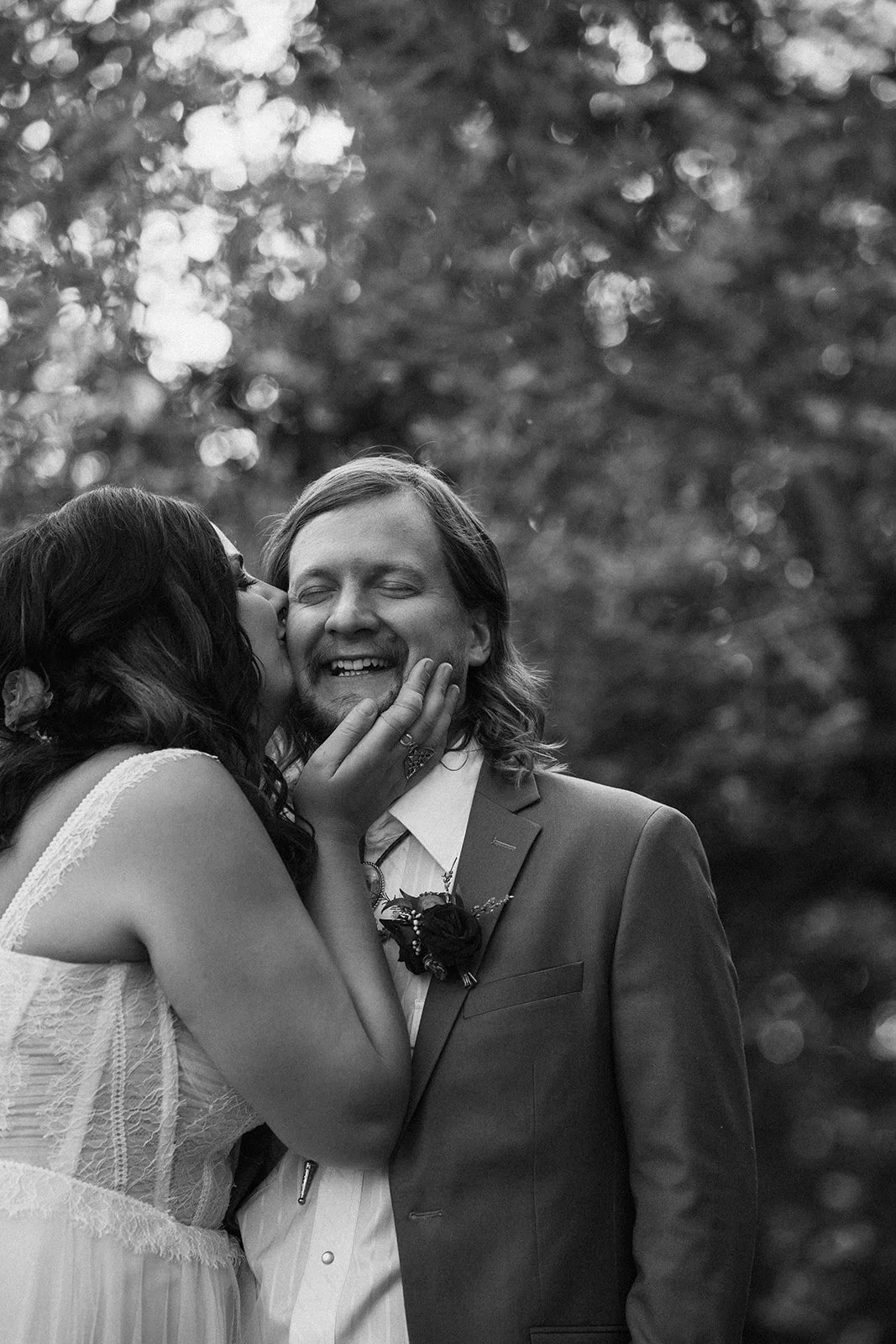 a bride kissing her groom on the cheek while he smiles with his eyes closed-thin-bordered
