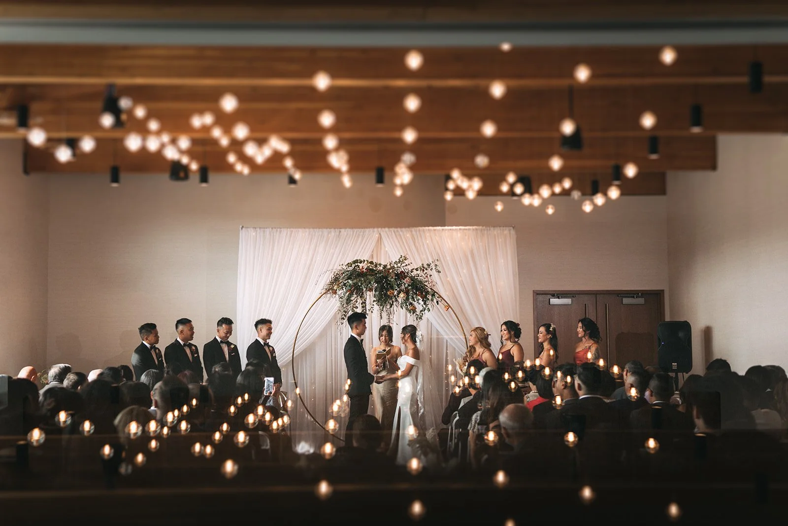 A couple stands at a circular altar holding hands and saying their vows. The lights from the venue are above, and reflected via a prism below