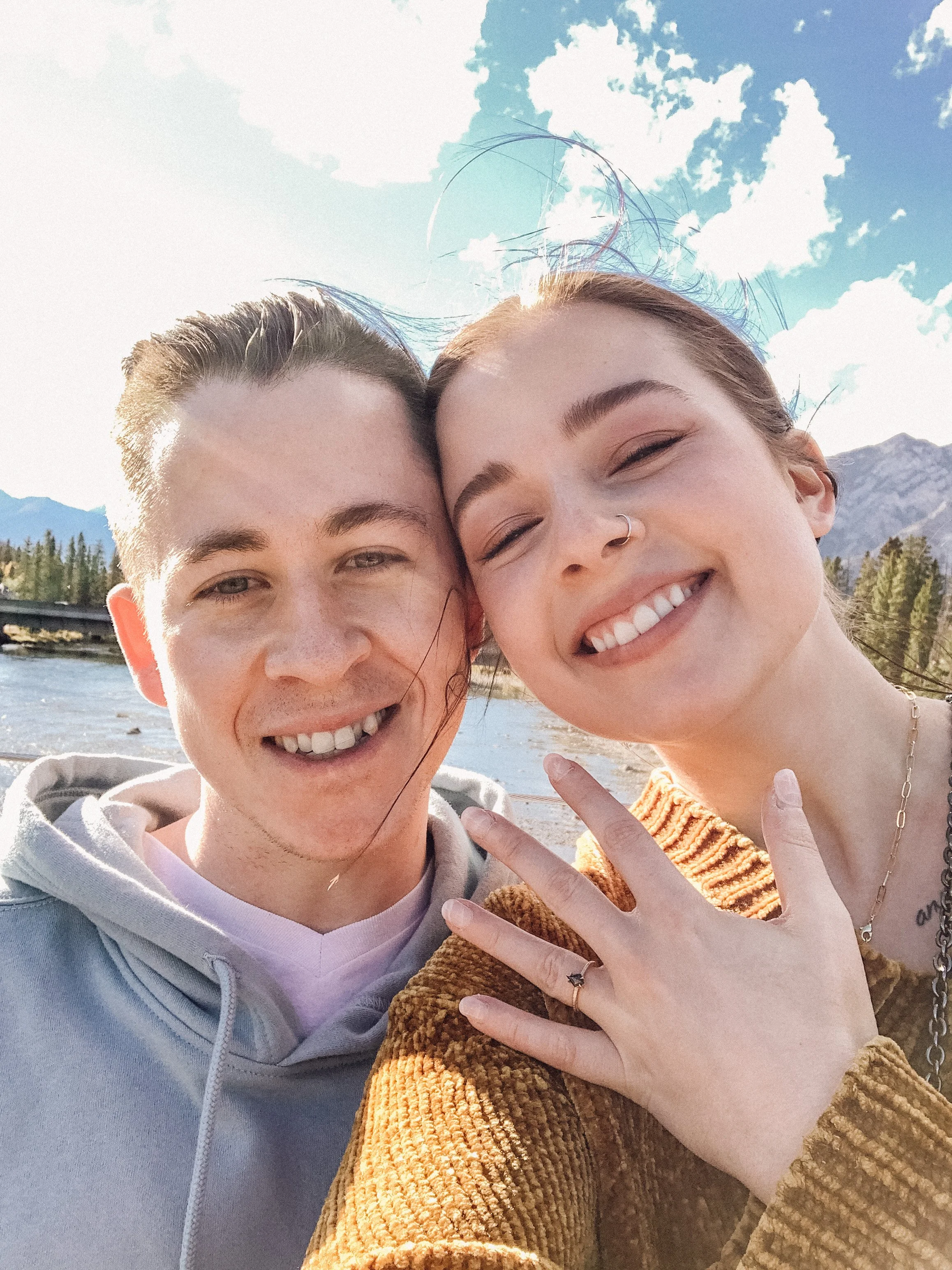 Janine Rose and her fiance smile at the camera as she holds up her left hand that has a black diamond ring on the ring finger