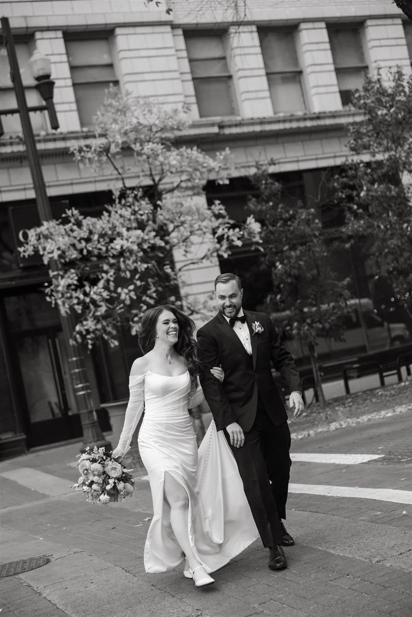 black and white photo of a bride and groom on a city street walking arm in arm and smiling-thin-bordered