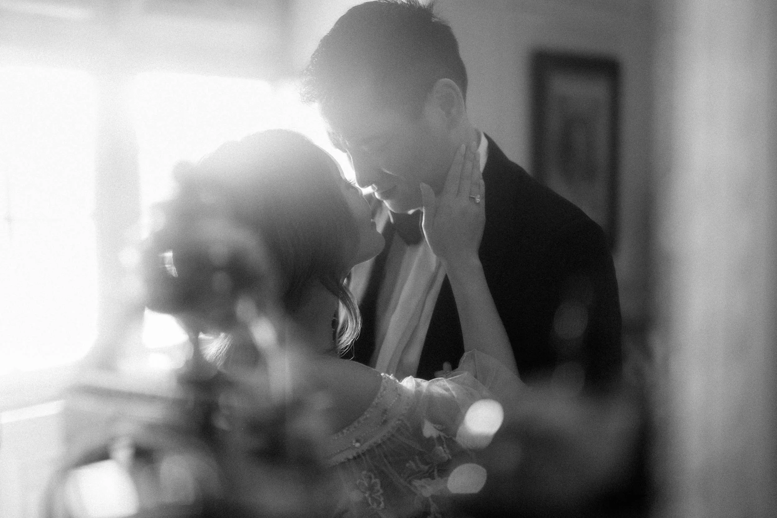 black and white photo of a bride holding her groom's cheek and smiling at one another-thin-bordered