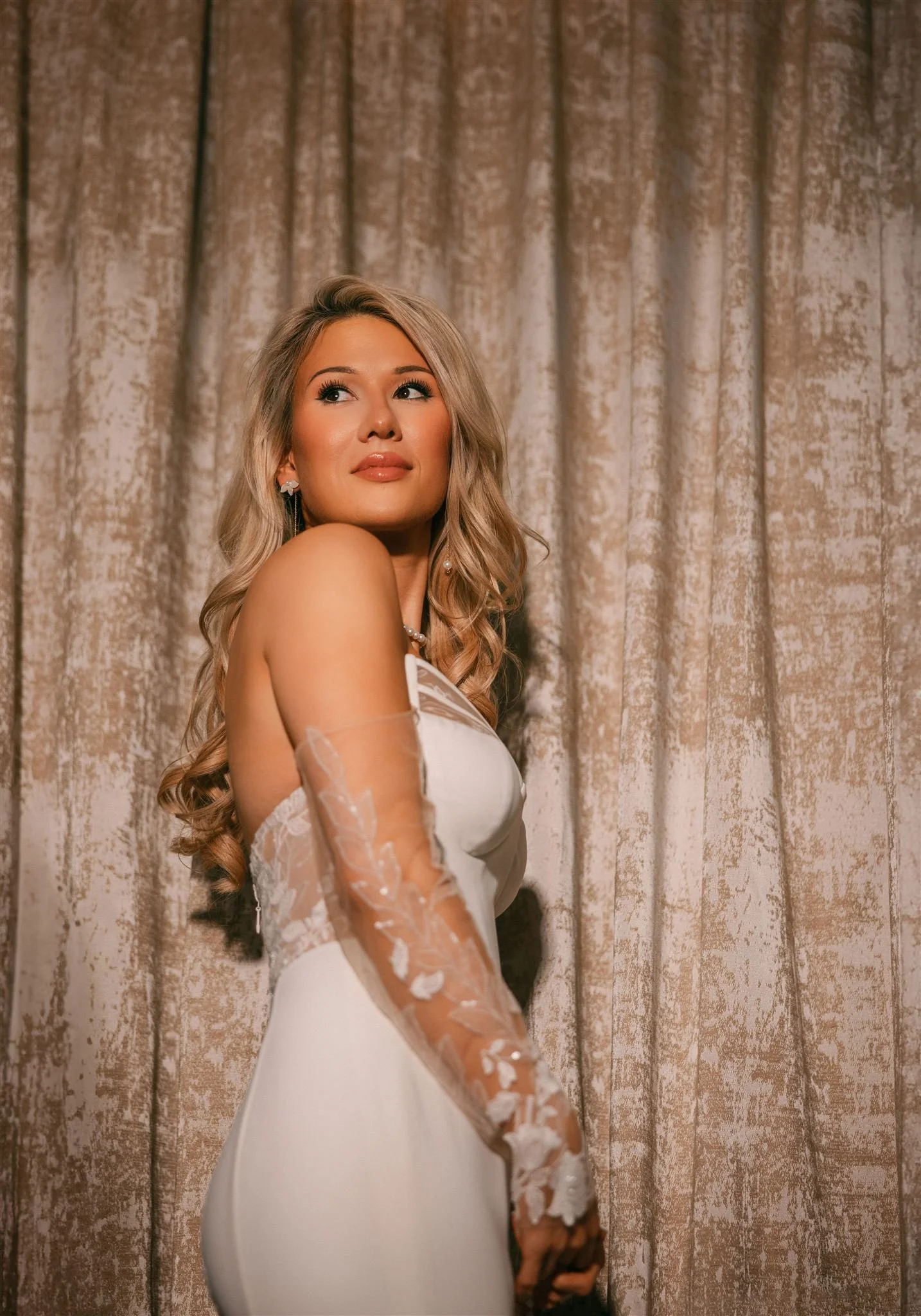 portrait of a bride looking over her shoulder against a glittery gold curtain-thin-bordered