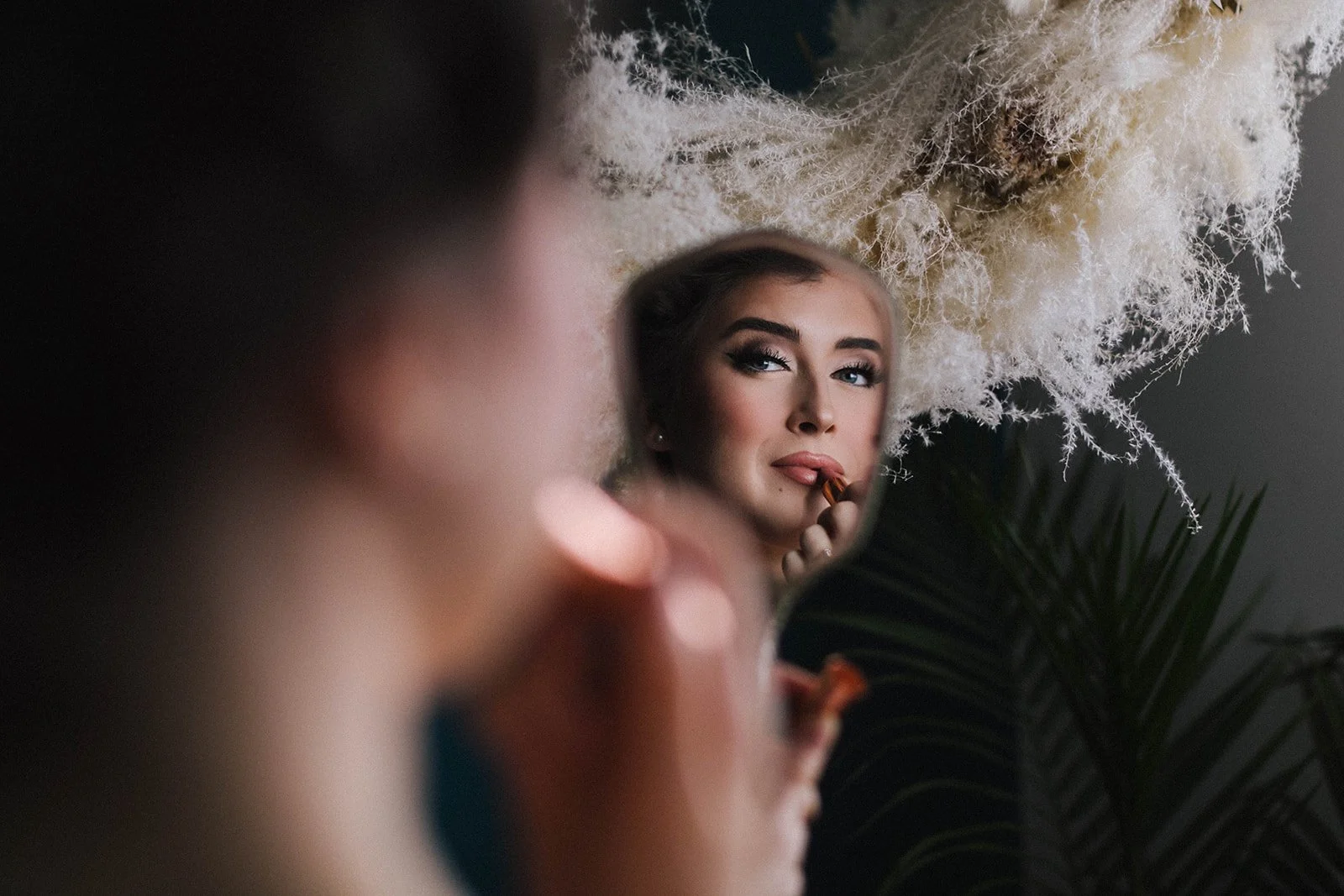 an over the shoulder shot of a woman applying pink lipstick in a vintage handheld mirror-thin-bordered