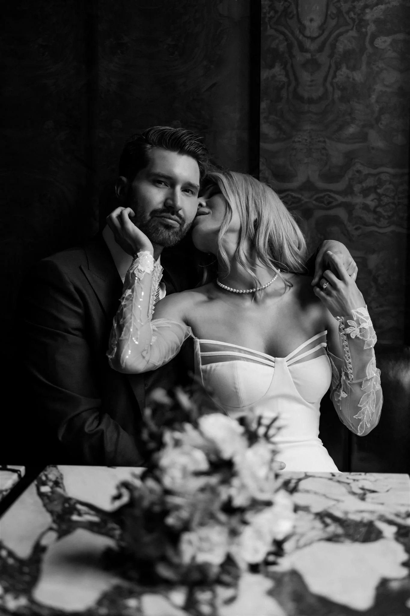 a bride and groom sitting in a restaurant booth and she's kissing his cheek