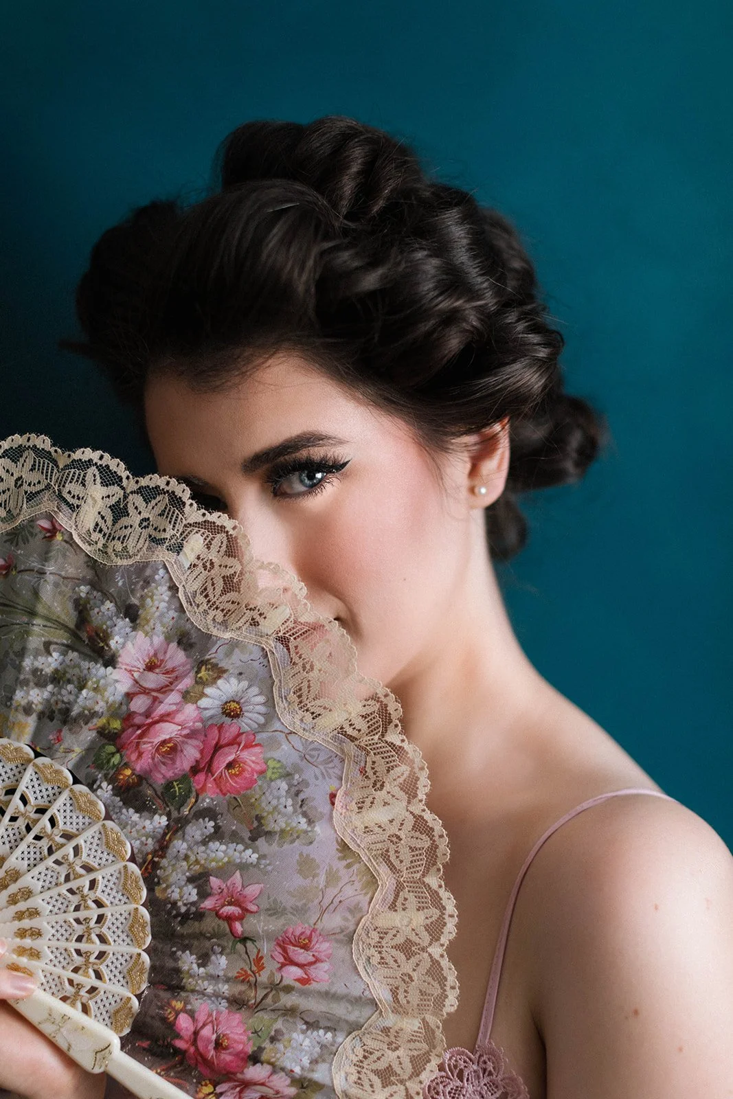 a woman gazing over a vintage lace fan with a teal backdrop