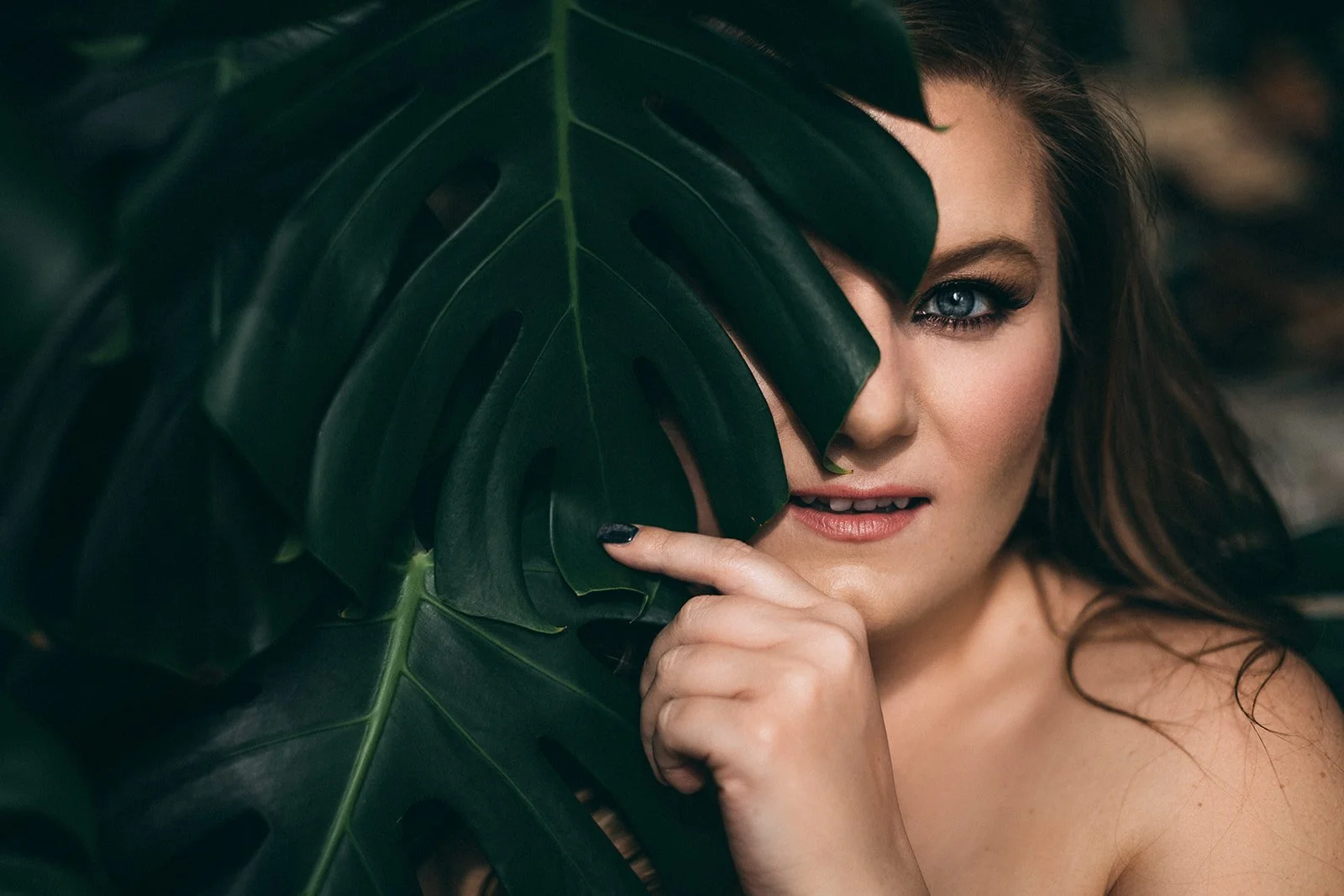 A woman peeks out from behind a large monstera leaf