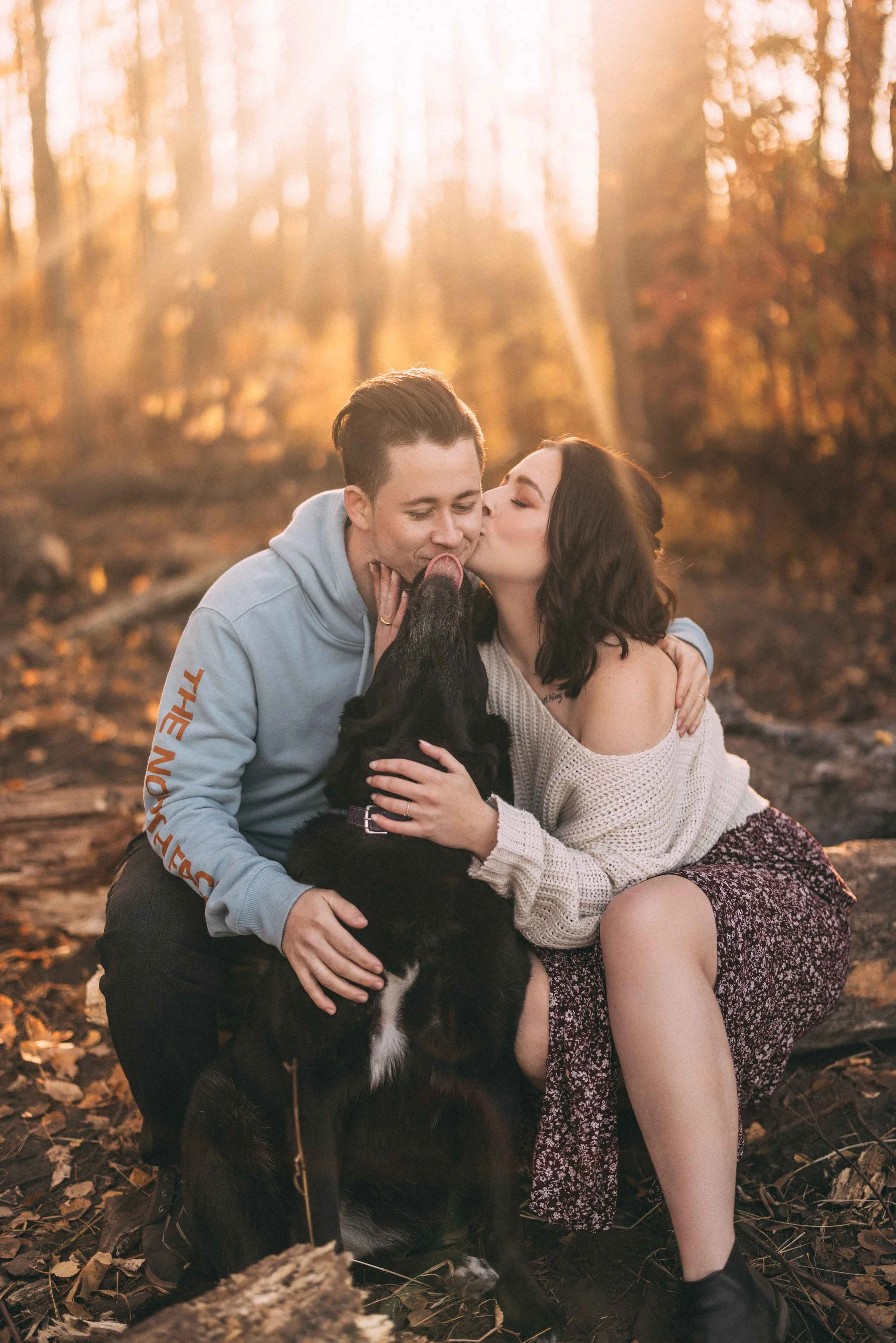 a couple in the woods in autumn being kissed by their dog-thin-bordered