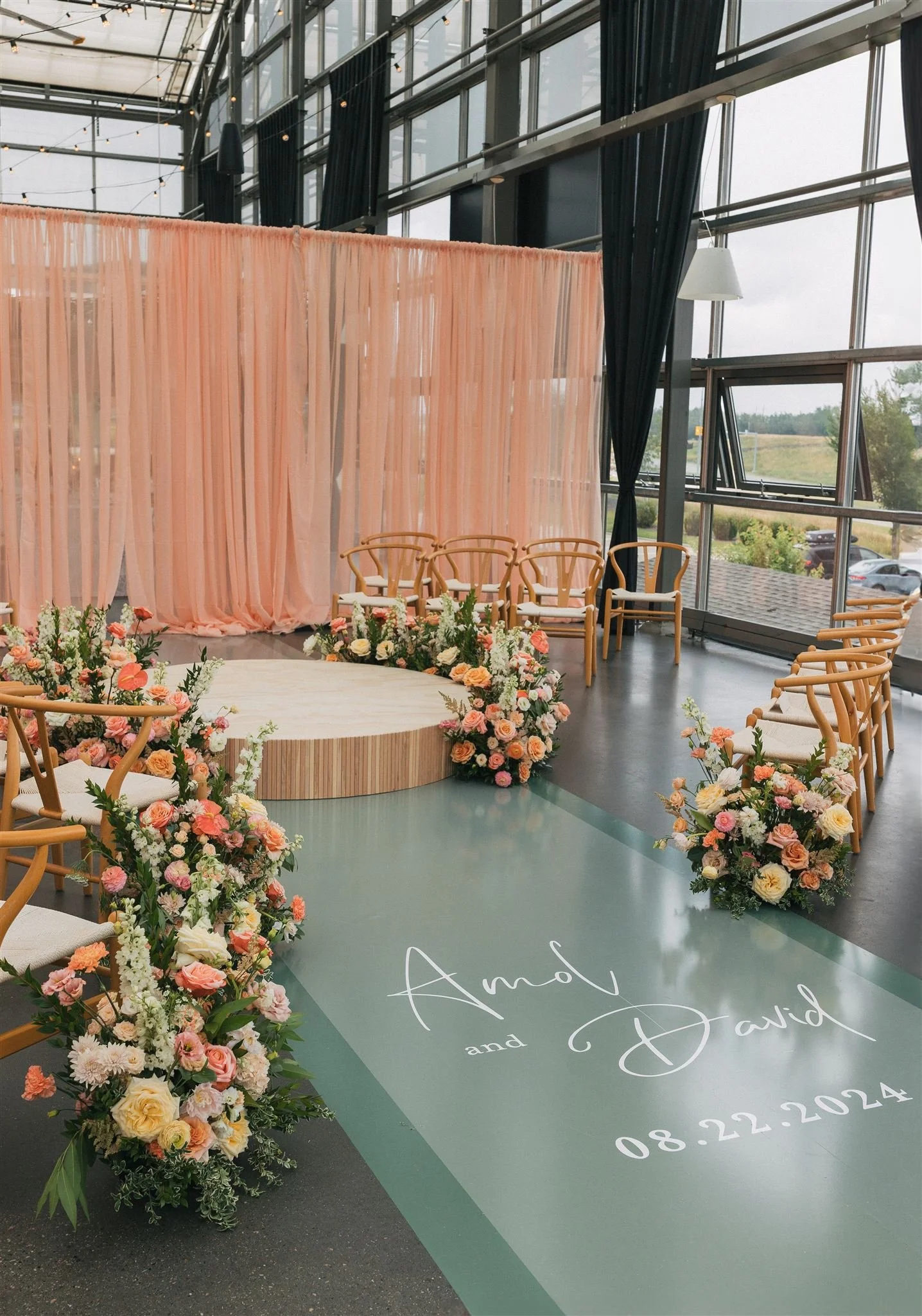 A wedding ceremony design featuring a circular wood platform for the couple to stand on, fully circled by chairs, vibrant peach and pink florals, and a custom vinyl aisle