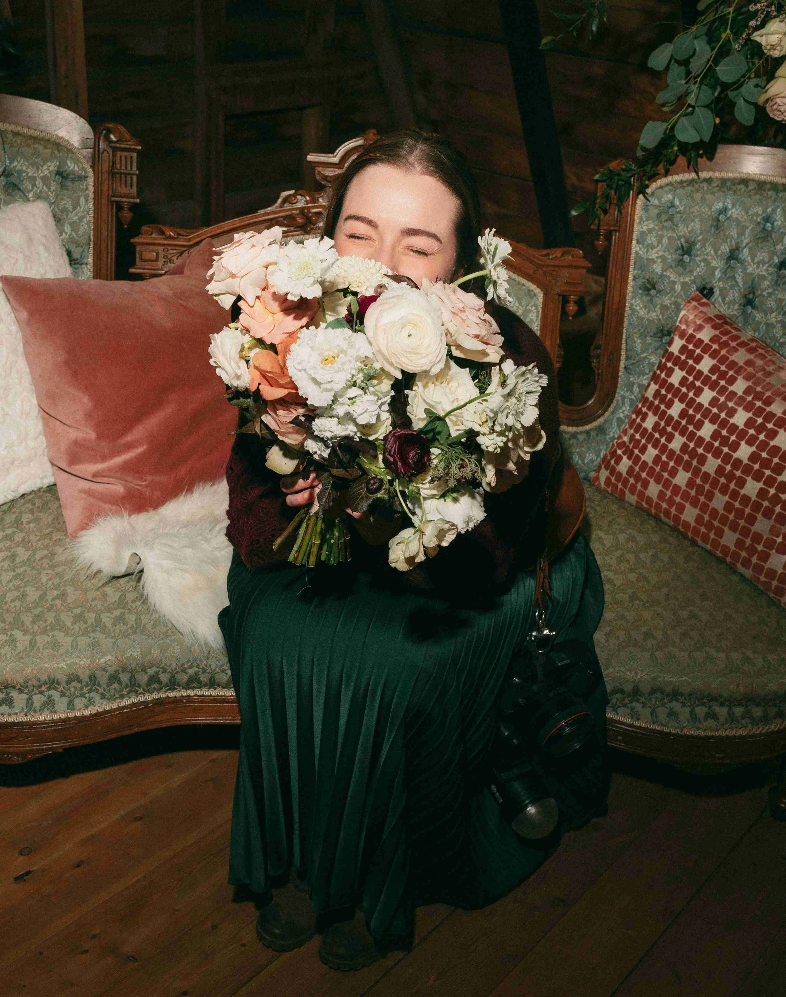 fun vintage style portrait of edmonton wedding photographer janine rose kneeling and holding a big bouquet of flowers in front of her face