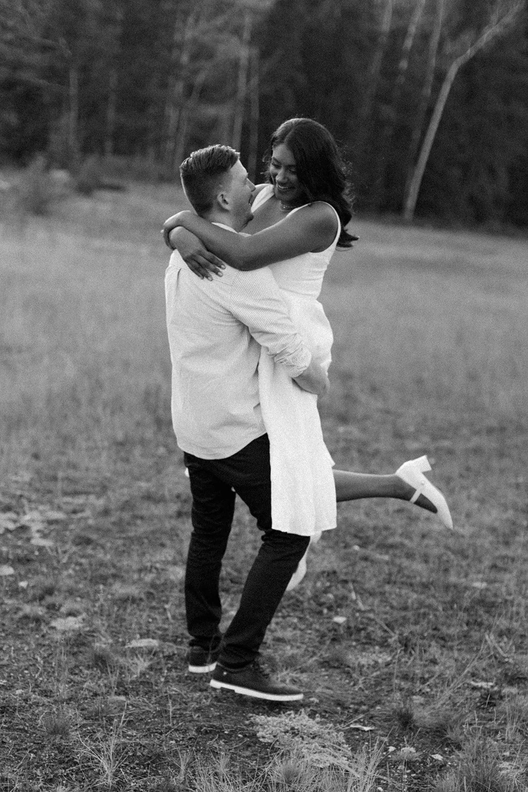 A man twirls his fiancee in a field in Banff, Alberta