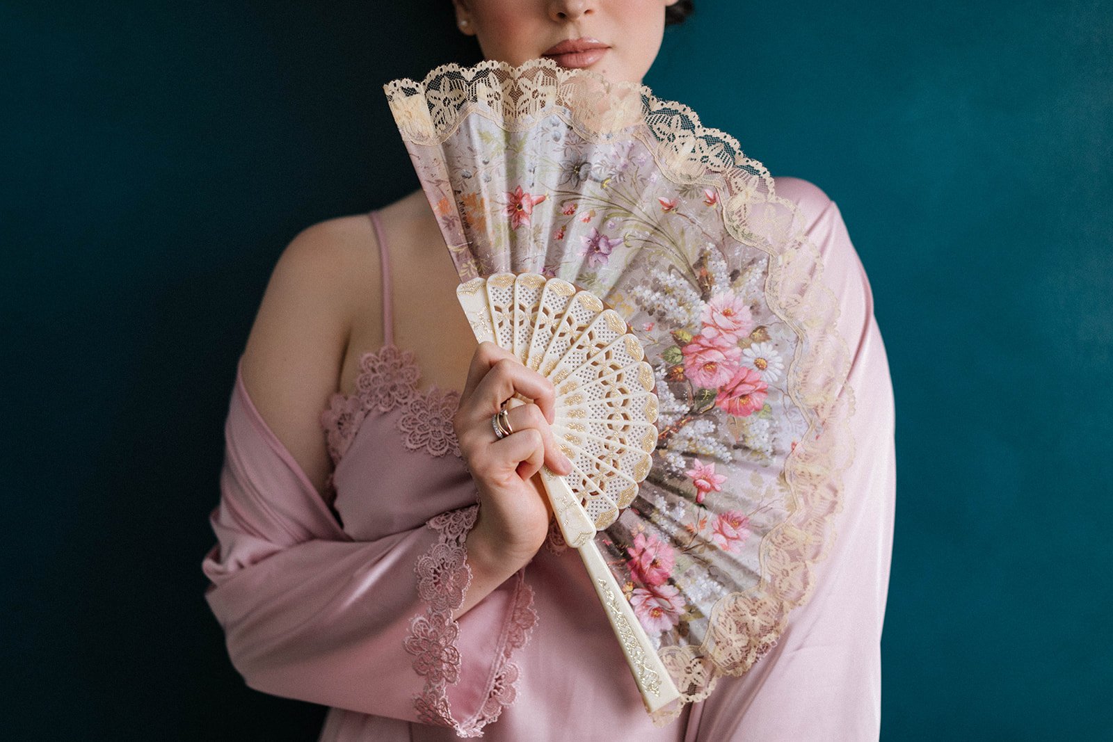 a woman wearing a pink floral nightie and robe holds a pink floral fan flirtaiously up to her face