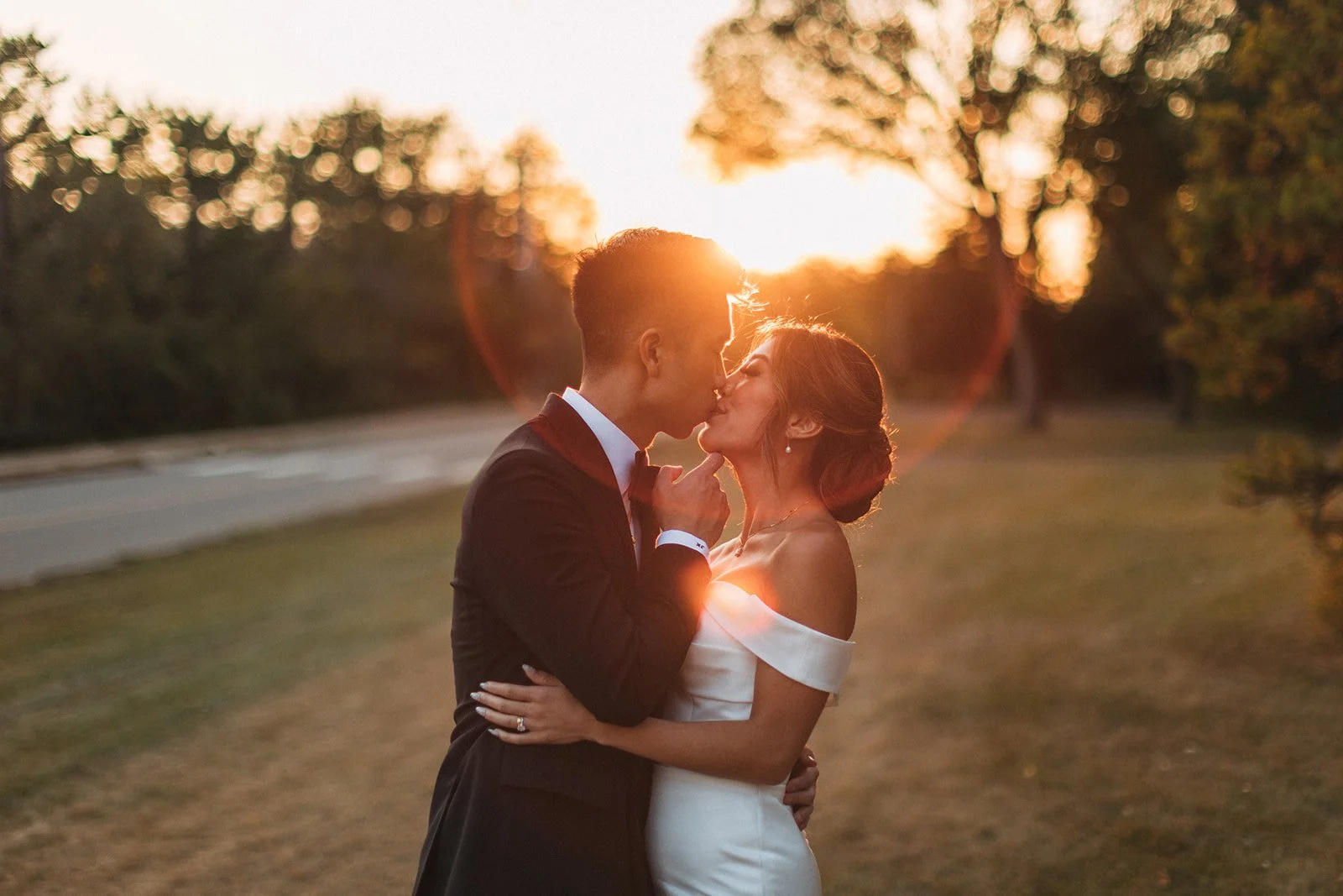 a couple shares a kiss at sunset, the sun flare makes a golen halo around their heads