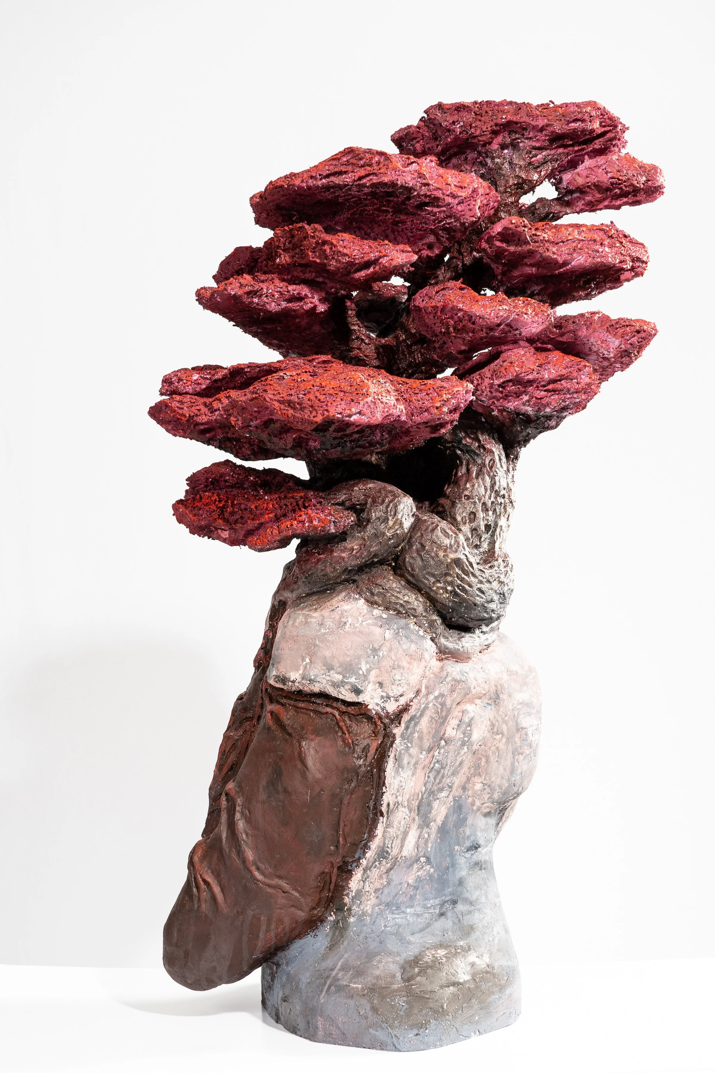 Sculpture resembling a tree with a textured gray trunk and large, layered red and purple leaves.