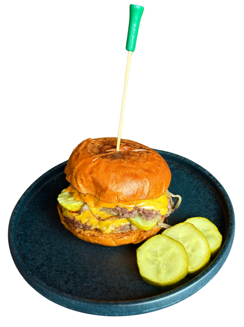 A cheeseburger with pickles on a bun, served on a dark plate with sliced pickles on the side.